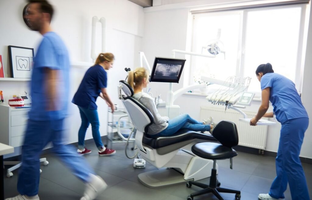 A woman sitting in a dental chair next to a screen with a dental imaging and dental team preparing for the treatment